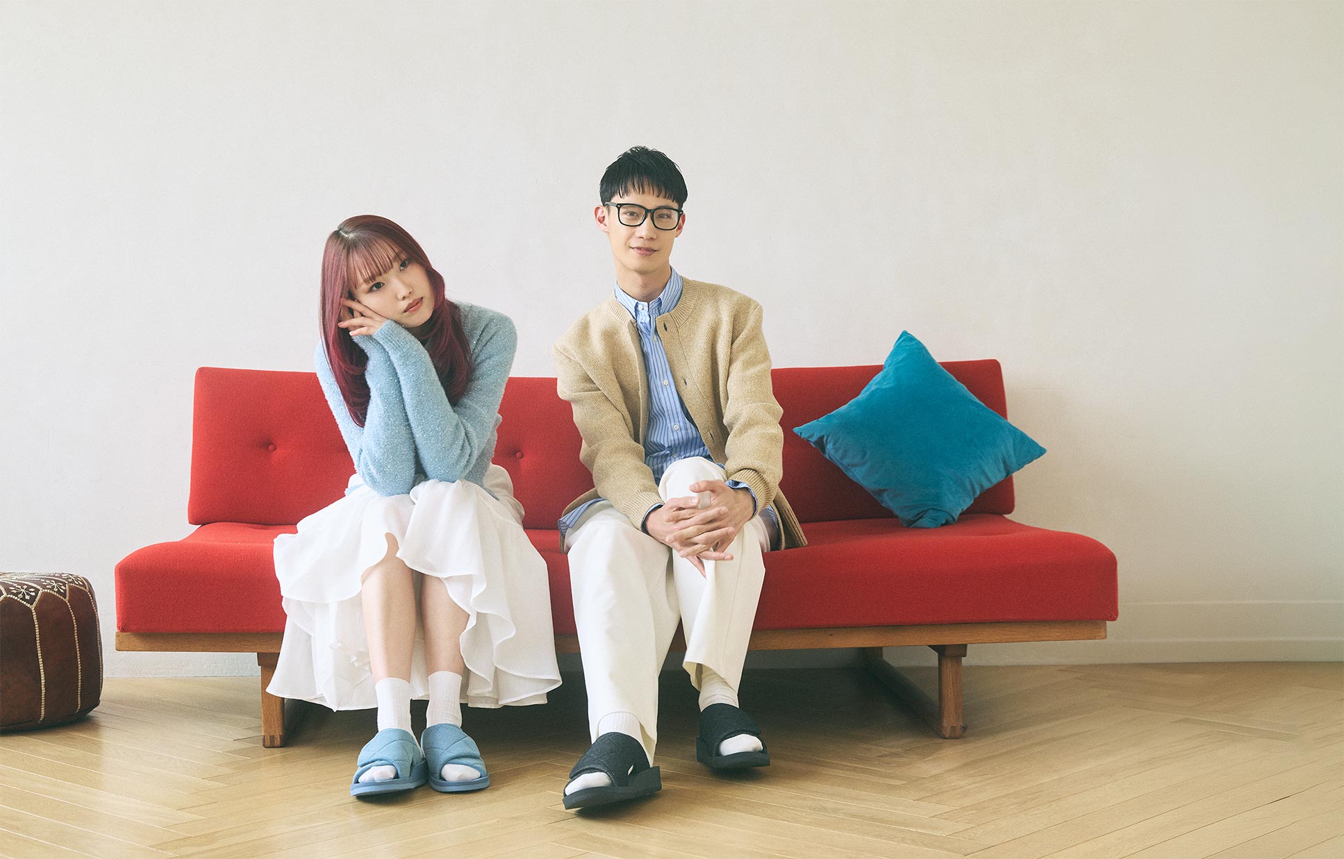 UTIPPA DENIM SAX BLUEを履いた女性と、DENIM BLACKを履いた男性が赤いソファに座ってくつろいでいる。